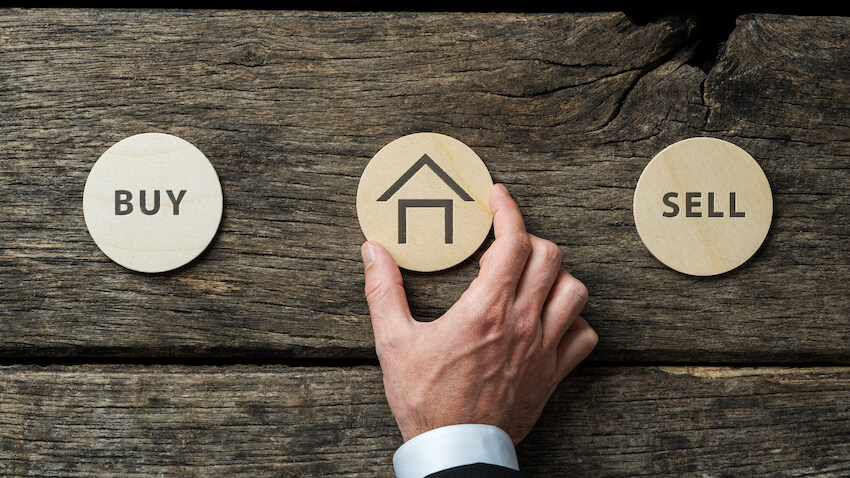 Real estate market conceptual image - hand of a businessman placing wooden cut circle with house shape on it in between Buy and Sell signs.